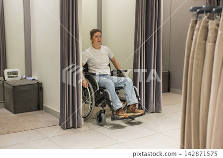 A Caucasian woman in a wheelchair is enters a fitting room. A Caucasian woman in a wheelchair is enters a fitting room. 142871575