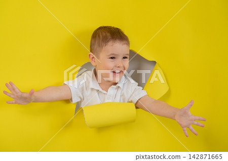 A mischievous boy tears apart a yellow paper background.  142871665