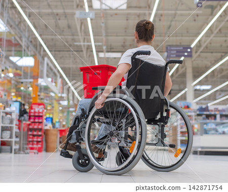 A Caucasian woman in a wheelchair shopping in a supermarket. A Caucasian woman in a wheelchair shopping in a supermarket. 142871754