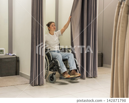 A Caucasian woman in a wheelchair is enters a fitting room. A Caucasian woman in a wheelchair is enters a fitting room. 142871798