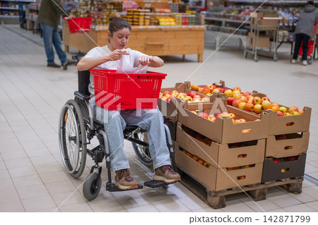 A Caucasian woman in a wheelchair buys apples at a supermarket. A Caucasian woman in a wheelchair buys apples at a supermarket. 142871799