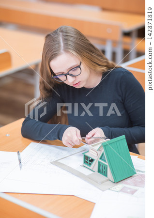 Caucasian young woman making a model of a building. Student of the construction university. Caucasian young woman making a model of a building. Student of the construction university. 142871819