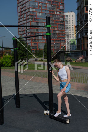 A Caucasian woman stretches her feet with a foam roller at a sports ground. 142872560