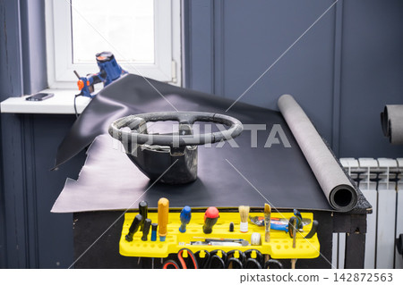 A seamstress in a workshop makes a new leather cover for a car steering wheel. 142872563