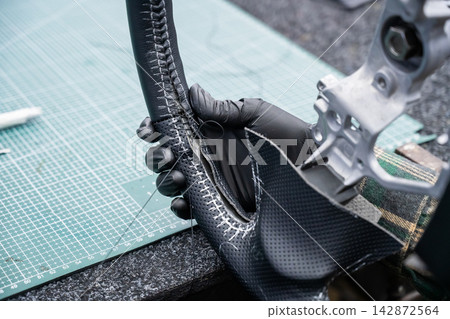 A seamstress in a workshop makes a new leather cover for a car steering wheel. 142872564