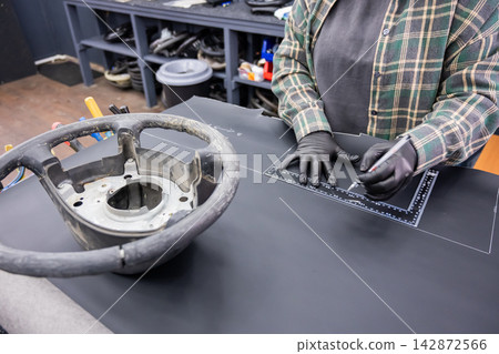 A seamstress in a workshop makes a new leather cover for a car steering wheel. A seamstress in a workshop makes a new leather cover for a car steering wheel. 142872566