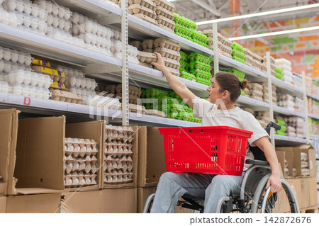 A Caucasian woman in a wheelchair shopping in a supermarket. A Caucasian woman in a wheelchair shopping in a supermarket. 142872676
