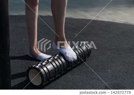 A Caucasian woman uses a foam roller to stretch her feet on a sports field. Close-up of her feet. A Caucasian woman uses a foam roller to stretch her feet on a sports field. Close-up of her feet. 142872779