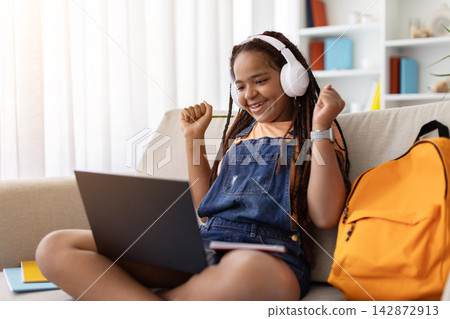 Excited Black teenage girl celebraing with raised fists while looking at laptop Excited Black teenage girl celebraing with raised fists while looking at laptop 142872913