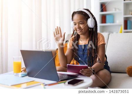 Teenage girl wearing headphones waving at laptop during video call at home Teenage girl wearing headphones waving at laptop during video call at home 142873051