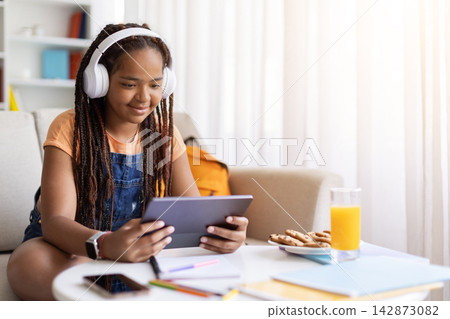 Black teenage girl wearing headphones using tablet for online learning at home Black teenage girl wearing headphones using tablet for online learning at home 142873082