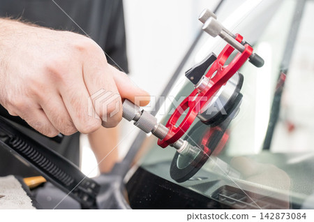 A technician injects resin into a windshield crack.  142873084