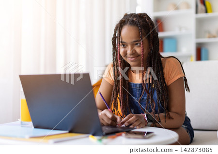 Black teenage girl studying at home with laptop, writing notes with pencil Black teenage girl studying at home with laptop, writing notes with pencil 142873085