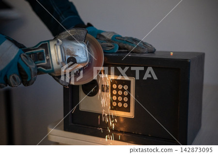 A man breaks into a safe with a grinder. A man breaks into a safe with a grinder. 142873095