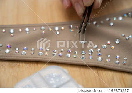 A woman decorates a gymnastics costume with rhinestones. Rhythmic gymnastics. Arranging with tweezers. A woman decorates a gymnastics costume with rhinestones. Rhythmic gymnastics. Arranging with tweezers. 142873227