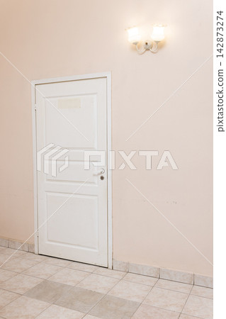 White door against soft pink painted wall with tiled floor and dual bulb wall lamp creating subtle retro interior atmosphere, minimalist design concept and pastel aesthetic background 142873274