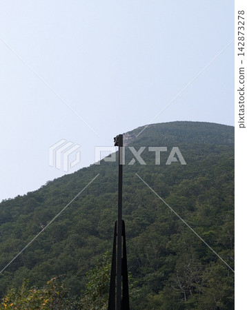 Modernist metal sculpture with a forested mountain background Modernist metal sculpture with a forested mountain background 142873278