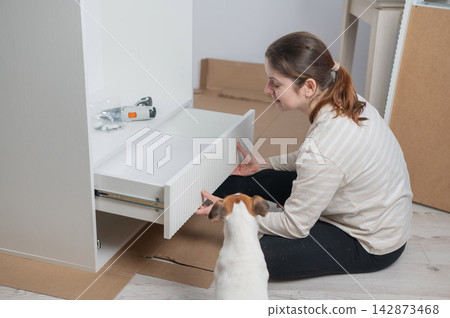 A Caucasian woman assembles furniture with her cute dog. A Caucasian woman assembles furniture with her cute dog. 142873468