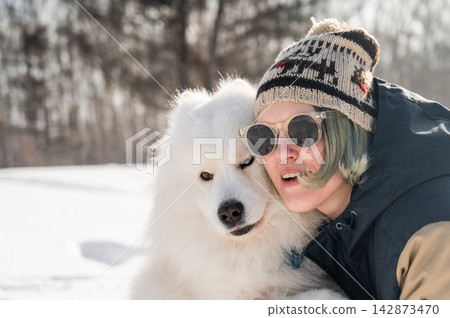 Portrait of a Smiling woman holding fluffy samoyed dog in snowy winter park. Portrait of a Smiling woman holding fluffy samoyed dog in snowy winter park. 142873470