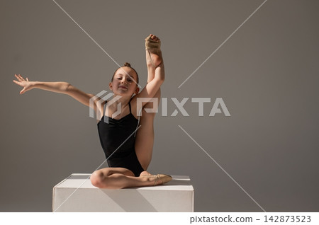 Little gymnast posing on a white cube on a white background. Little gymnast posing on a white cube on a white background. 142873523