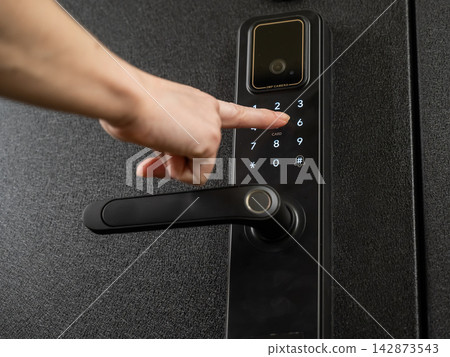 A woman opens a modern smart door lock with a digital keypad using a code. A woman opens a modern smart door lock with a digital keypad using a code. 142873543
