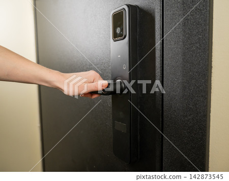 A woman opens a modern smart door lock with a digital keypad and biometric fingerprint access. A woman opens a modern smart door lock with a digital keypad and biometric fingerprint access. 142873545