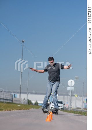 A Caucasian man rollerblades around the slalom course. A Caucasian man rollerblades around the slalom course. 142873554