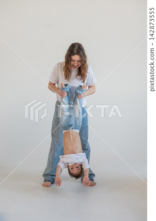 A Caucasian woman holds her two-year-old son by the legs. The boy and mother are playing around. A Caucasian woman holds her two-year-old son by the legs. The boy and mother are playing around. 142873555