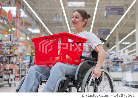 A Caucasian woman in a wheelchair shopping in a supermarket. A Caucasian woman in a wheelchair shopping in a supermarket. 142873565