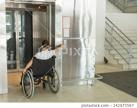 A Caucasian woman in a wheelchair uses an elevator. A Caucasian woman in a wheelchair uses an elevator. 142873567