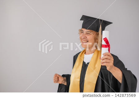 Happy senior woman in graduation gown holding diploma on white background. Happy senior woman in graduation gown holding diploma on white background. 142873569