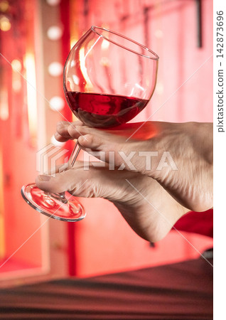 Foot fetish. A woman holds a glass of red wine with her feet. Foot fetish. A woman holds a glass of red wine with her feet. 142873696