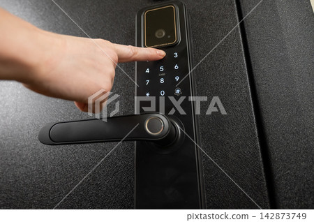 A woman opens a modern smart door lock with a digital keypad using a code. A woman opens a modern smart door lock with a digital keypad using a code. 142873749