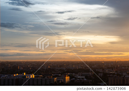 Serene sunset sky with golden cloud layer over city skyline creates peaceful evening atmosphere across vast urban landscape panorama 142873906