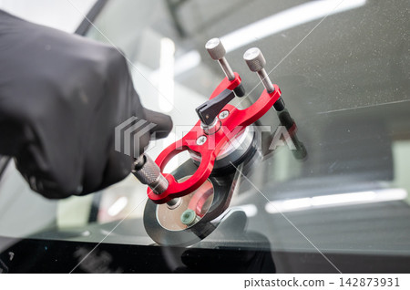 A technician injects resin into a windshield crack. A technician injects resin into a windshield crack. 142873931
