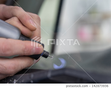 A technician drills a hole during a car windshield chip repair. A technician drills a hole during a car windshield chip repair. 142873936