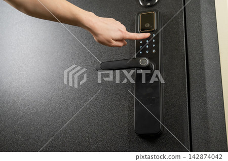 A woman opens a modern smart door lock with a digital keypad using a code. A woman opens a modern smart door lock with a digital keypad using a code. 142874042