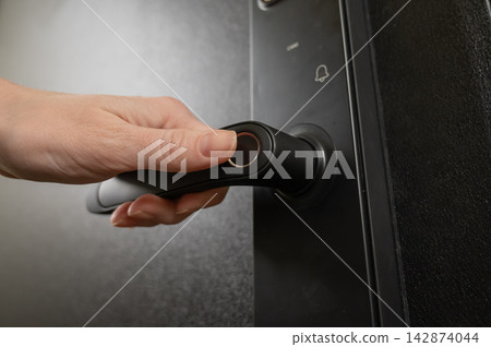 A woman opens a modern smart door lock with a digital keypad and biometric fingerprint access. A woman opens a modern smart door lock with a digital keypad and biometric fingerprint access. 142874044