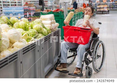 A Caucasian woman in a wheelchair shopping in a supermarket. A Caucasian woman in a wheelchair shopping in a supermarket. 142874049