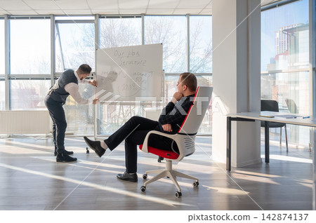 Two Caucasian men discussing work at a white board. Two Caucasian men discussing work at a white board. 142874137