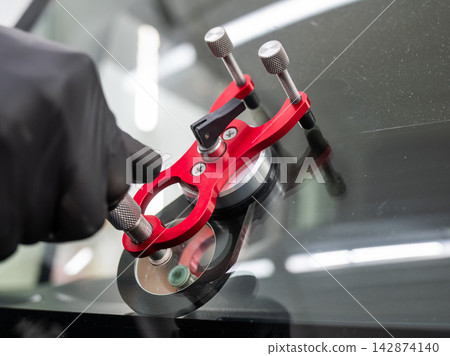 A technician injects resin into a windshield crack.  142874140
