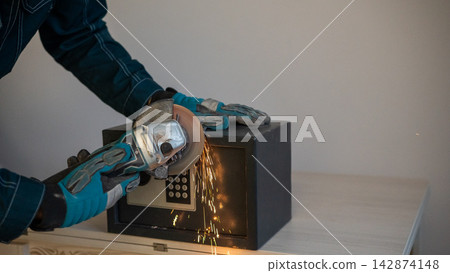 A man breaks into a safe with a grinder. A man breaks into a safe with a grinder. 142874148