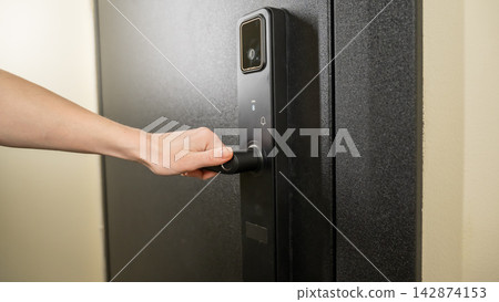 A woman opens a modern smart door lock with a digital keypad and biometric fingerprint access. A woman opens a modern smart door lock with a digital keypad and biometric fingerprint access. 142874153