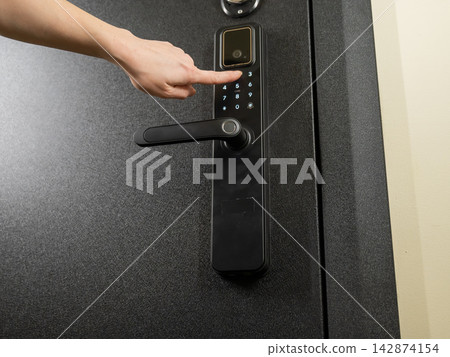 A woman opens a modern smart door lock with a digital keypad using a code. A woman opens a modern smart door lock with a digital keypad using a code. 142874154