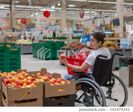 A Caucasian woman in a wheelchair buys apples at a supermarket. 142874242