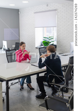 Man and woman talking while sitting at desk in office. Man and woman talking while sitting at desk in office. 142874269