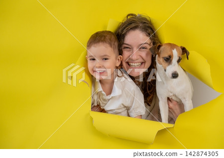 Caucasian little boy, his mother and Jack Russell Terrier dog tearing yellow paper background. Caucasian little boy, his mother and Jack Russell Terrier dog tearing yellow paper background. 142874305