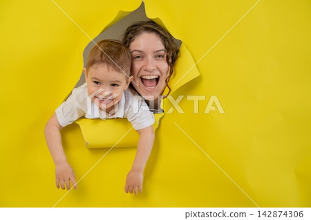 Caucasian little boy and his mother tearing yellow paper background. Caucasian little boy and his mother tearing yellow paper background. 142874306