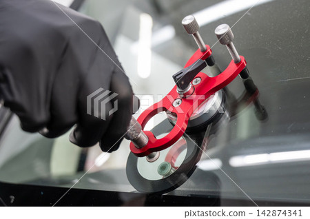 A technician injects resin into a windshield crack. A technician injects resin into a windshield crack. 142874341