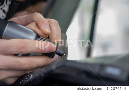 A technician drills a hole during a car windshield chip repair. 142874344